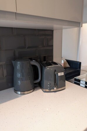Eine Küchenzeile mit Wasserkocher, Toaster und einer dunkel gefliesten Spritzschutzwand.