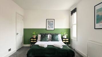 A bedroom with a bed, two bedside tables, a window, and a framed picture on the wall.