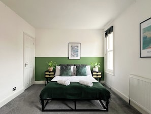 Une chambre à coucher avec un lit, deux tables de chevet, une fenêtre et un tableau encadré au mur.