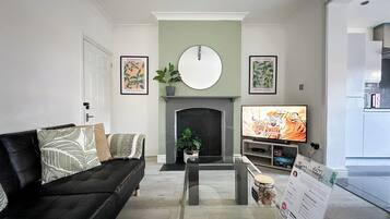 A living room with a fireplace, a black sofa, a television, and a welcome sign.