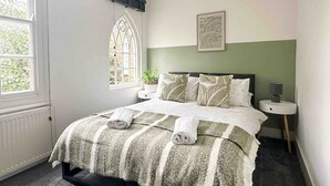 Una camera da letto con un letto, una finestra, un comodino e un'opera d'arte appesa al muro.