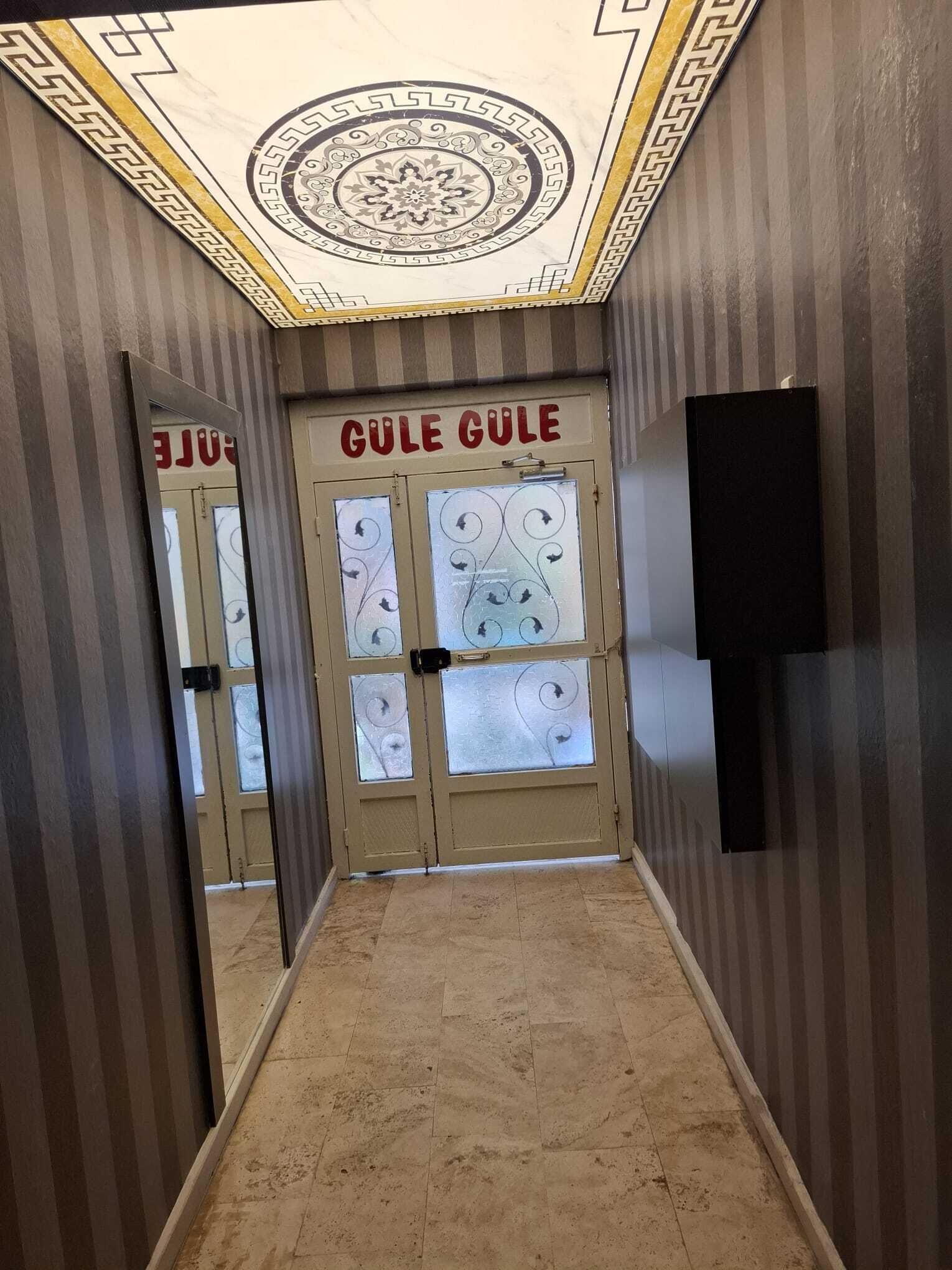 A hallway with striped walls, a mirrored door with 'GULE GULE' signage, and a tiled floor.