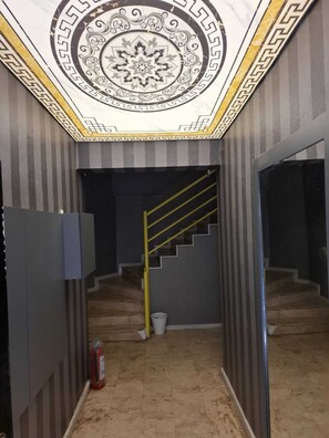 A hallway with a decorative ceiling, a staircase with yellow handrails, and a fire extinguisher on the floor.