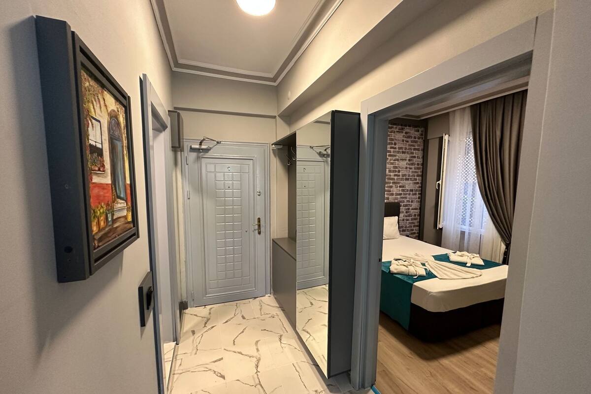 A hallway with a marble floor, a door with a grid pattern, and a bed with a green bedspread and white towels.