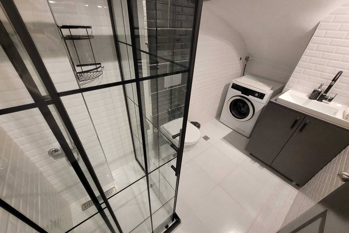 A modern bathroom with a glass shower enclosure, a washing machine, and a sink with a mirror.