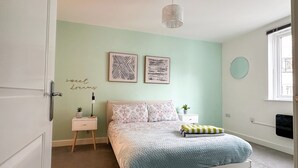 A bedroom with a bed, bedside tables, a wall clock, and artwork.