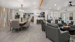 A spacious living area with a dining table, sofas, and a kitchen in the background. - Private Pickleball, B-Ball, Putt, Pool, Spa, Grill (Scottsdale)