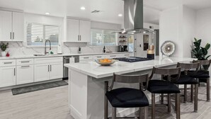A modern kitchen with white cabinetry, a central island with bar stools, and a stainless steel range hood. - Private Pickleball, B-Ball, Putt, Pool, Spa, Grill (Scottsdale)
