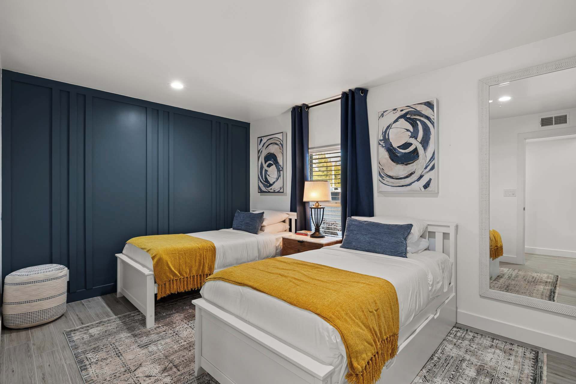 A bedroom with two beds, a nightstand, a lamp, and artwork on the walls.