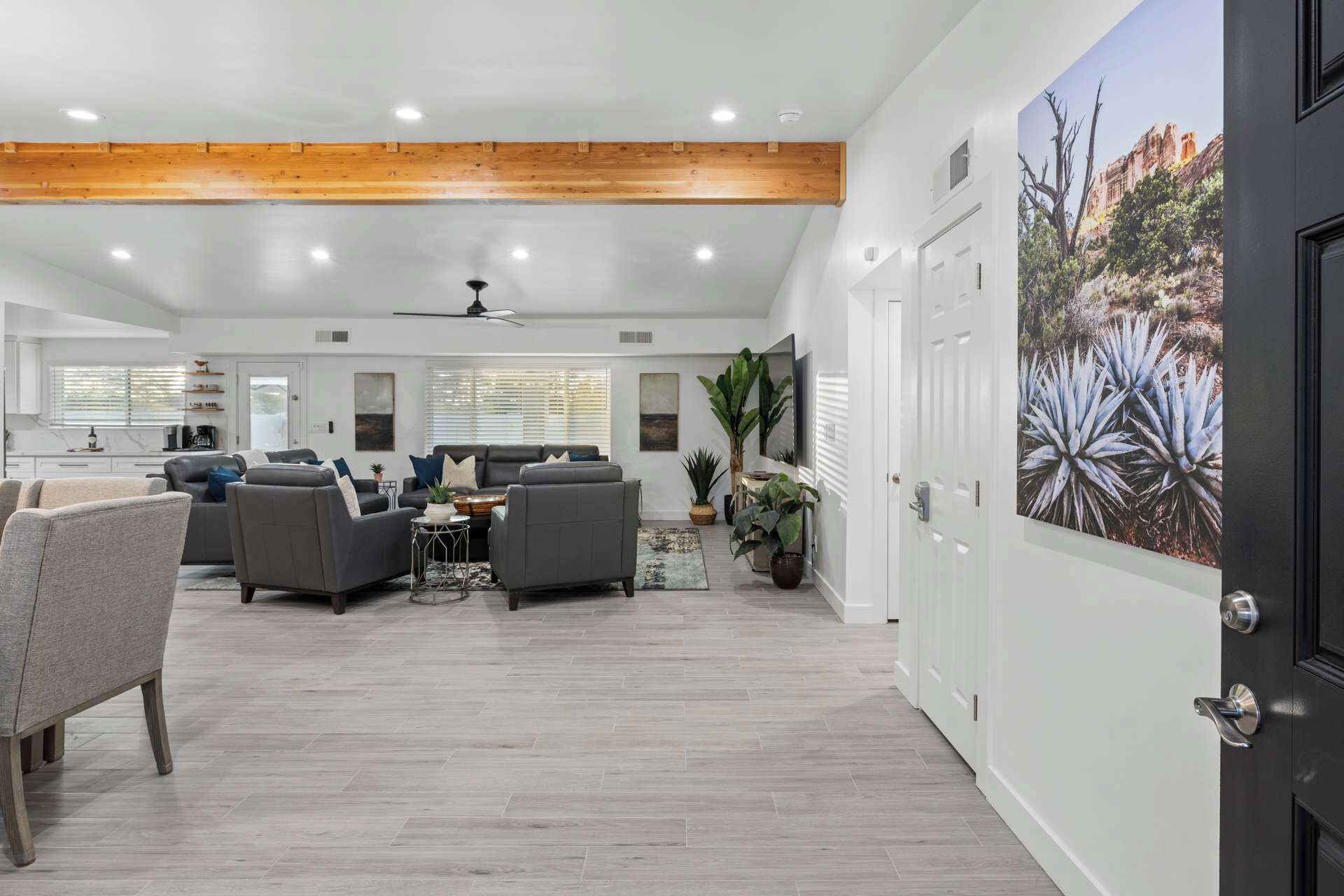 A spacious living area with a high ceiling, a kitchen in the background, and a large door with a plant and artwork.