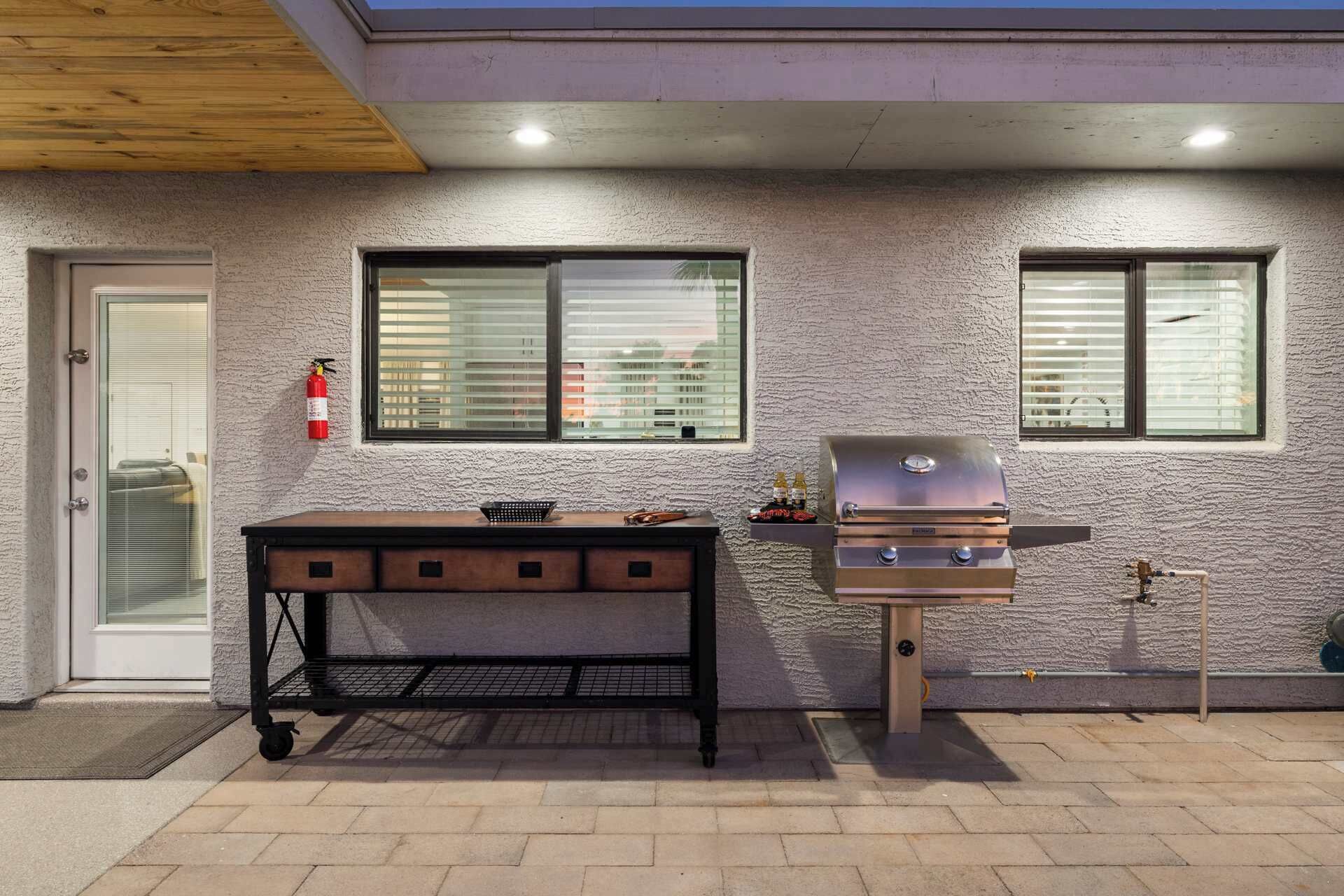 Terrassa exterior amb una barbacoa, una taula amb una cistella i un extintor.