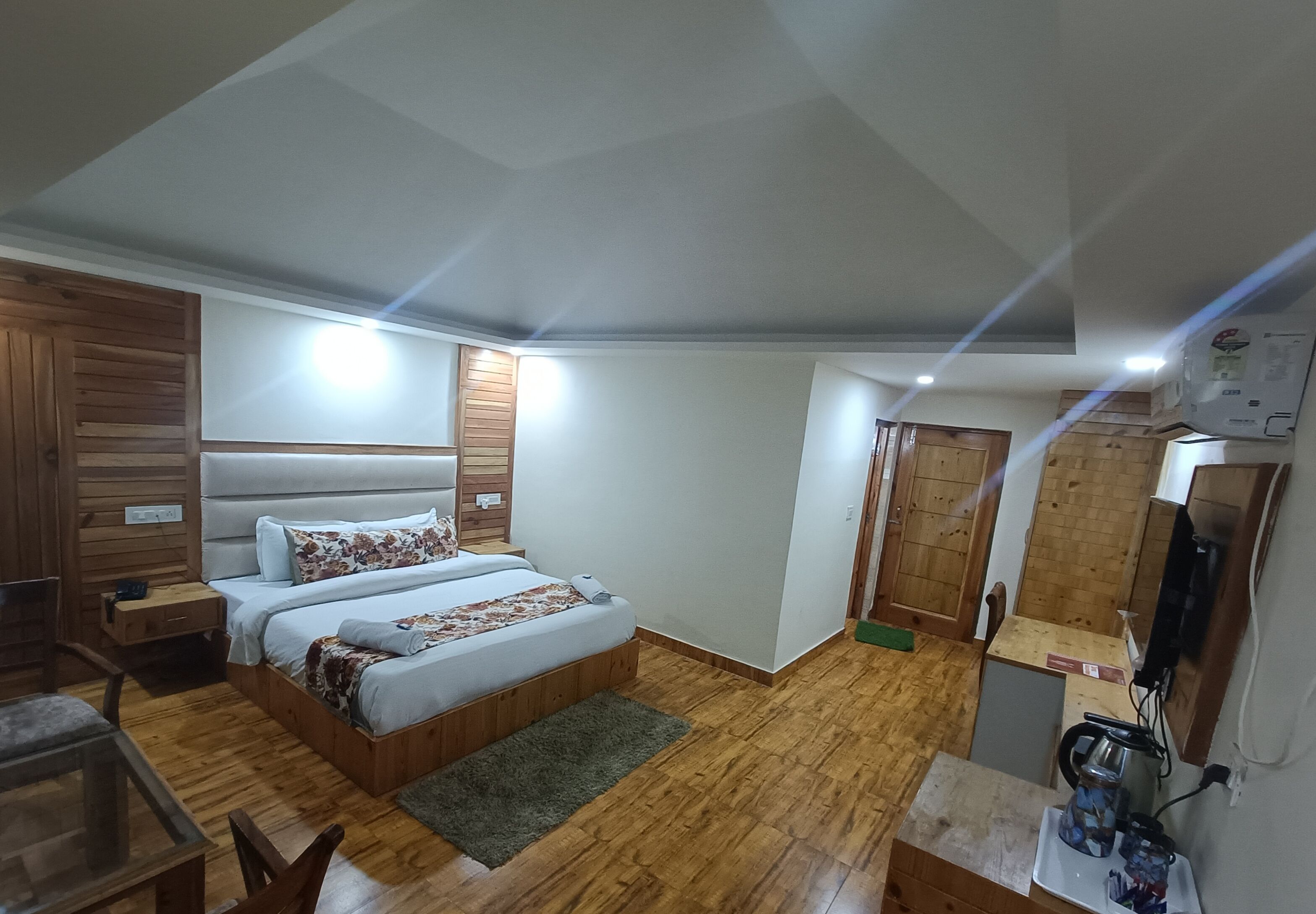 Un dormitorio con piso de madera, una cama con colcha estampada, una mesita de noche, un escritorio con silla y un televisor.