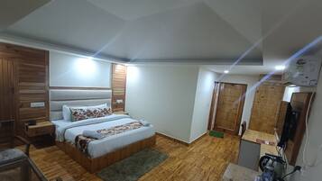 Un dormitorio con piso de madera, una cama con colcha estampada, una mesita de noche, un escritorio con silla y un televisor.