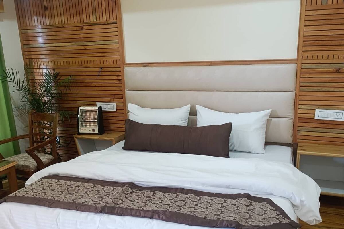 A neatly made bed with a patterned throw, wooden headboard, and a bedside table with a heater.