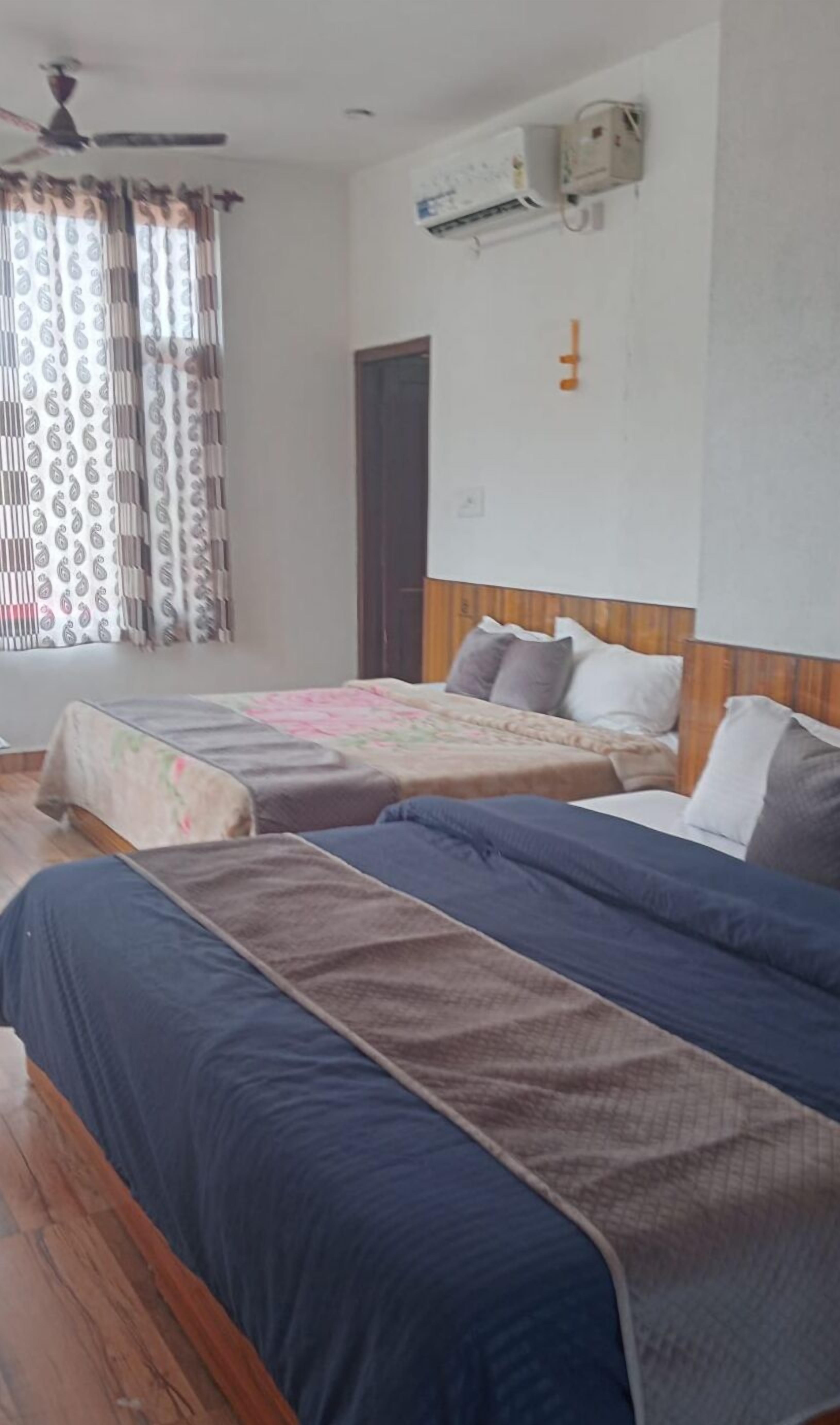 Una camera d'albergo con due letti, una ventola a soffitto, un condizionatore d'aria e una finestra con tende decorate.