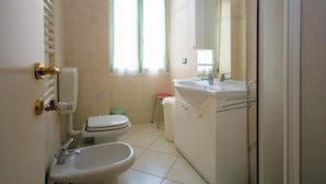 A bathroom with a toilet, bidet, sink, and a window with curtains. - Europa 29 Trilocale Manhattan (Loano)