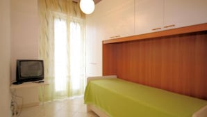 A small, simple room with a bed, a television, and a window with curtains. - Europa 29 Trilocale Manhattan (Loano)