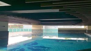 An indoor swimming pool with clear water, tiled floor, and a modern ceiling design. - Capital O 93636 La Grande Apartment By UJM (Bandung)