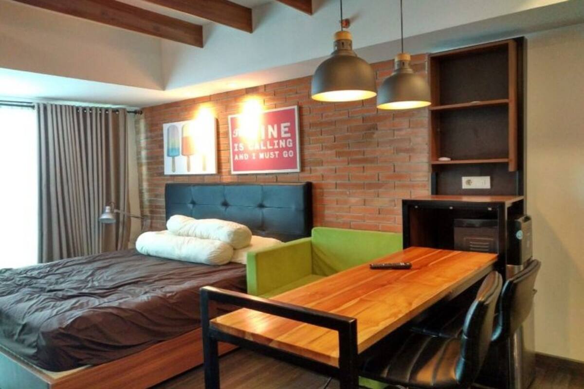A modern room with a bed, a green chair, a wooden table, and a brick wall with a sign.