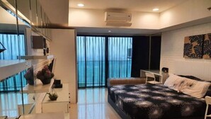 A modern bedroom with a large bed, a desk, and a view of the sea through floor-to-ceiling windows. - Capital O 93636 La Grande Apartment By UJM (Bandung)
