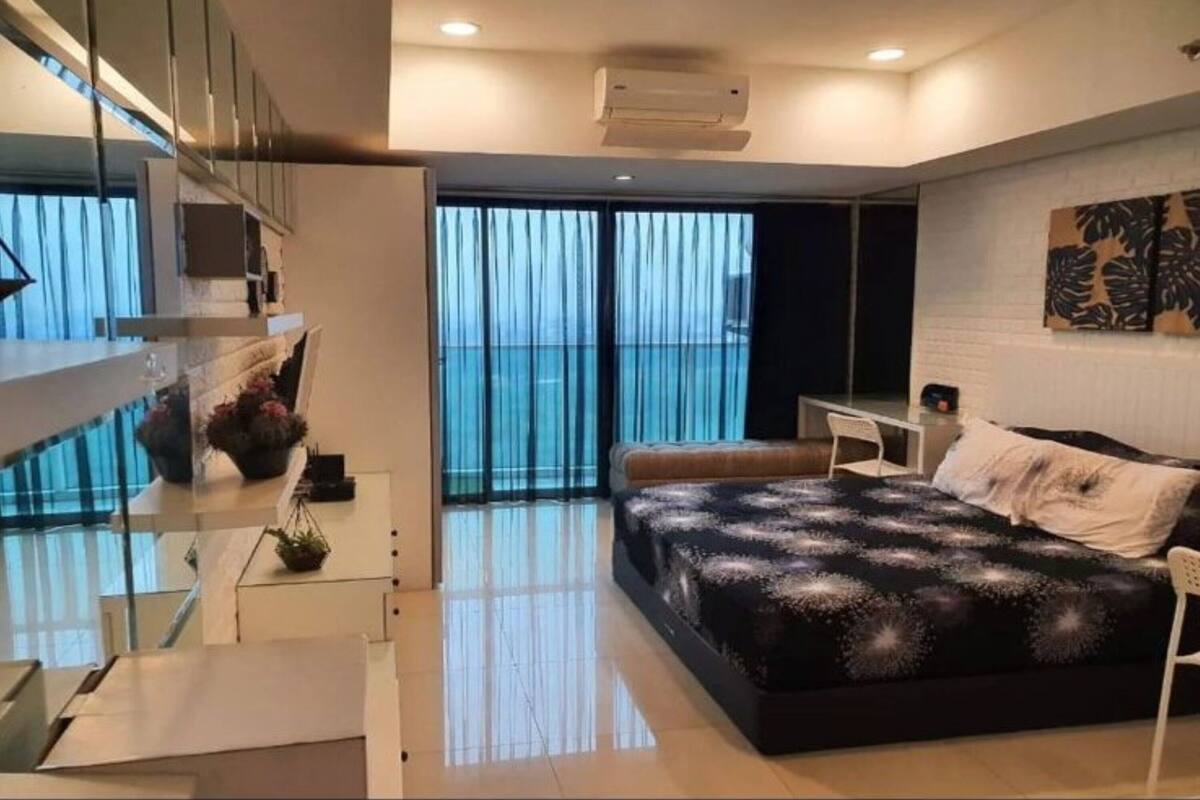 A modern bedroom with a large bed, a desk, and a view of the sea through floor-to-ceiling windows.