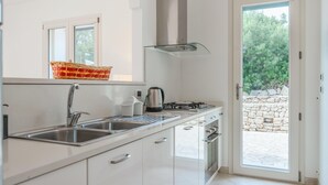 A modern kitchen with a stainless steel sink, a gas stove, and a built-in oven. There is a window above the sink and a door leading to an outdoor area. - Villa Donna Eleonora - Alloggio Stella Marina (Morciano di Leuca)