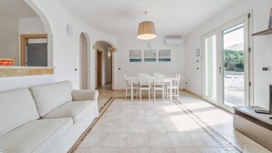 A modern living room with a sofa, dining table, and chairs, a ceiling light, and a view through a glass door. - Villa Donna Eleonora - Alloggio Stella Marina (Morciano di Leuca)