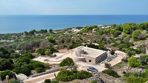 Ein Küstenhaus mit Steinfassade, umgeben von viel Grün und Blick auf das Meer.