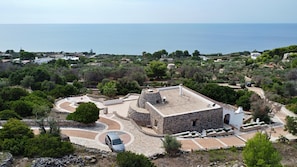 Un bâtiment en pierre doté d’une cour intérieure circulaire, entouré de verdure et offrant une vue sur la mer.