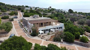 Une villa moderne dotée d’un vaste patio, d’un chemin en pierre menant à l’entrée et offrant une vue sur la mer.