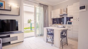 A modern kitchen with a built-in microwave, stove, and overhead ventilation. There is a dining area with a table and chairs, and a TV mounted on the wall. - Il Vento del Sud - Italian Homing (Padenghe sul Garda)