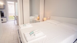 A hotel room with a large bed, a bedside table with lamps, a TV, and a bathroom visible through an open door. - Il Vento del Sud - Italian Homing (Padenghe sul Garda)