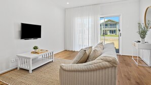 A modern living room with a flat-screen TV, a white console table, a beige sofa, and a large window with curtains.