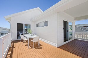 Ein weißes Gebäude mit einer Holzterrasse, einem Tisch und Stühlen sowie einer Schiebeglastür.