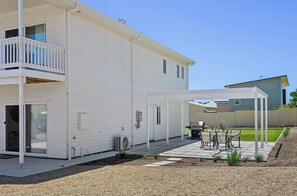 Ein weißes, zweistöckiges Haus mit überdachter Terrasse, Balkon und kleinem Garten.