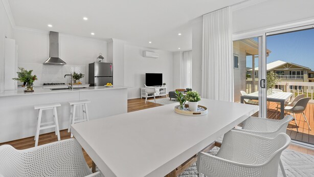 A modern kitchen with white cabinetry, a central island, and a dining area with white chairs.