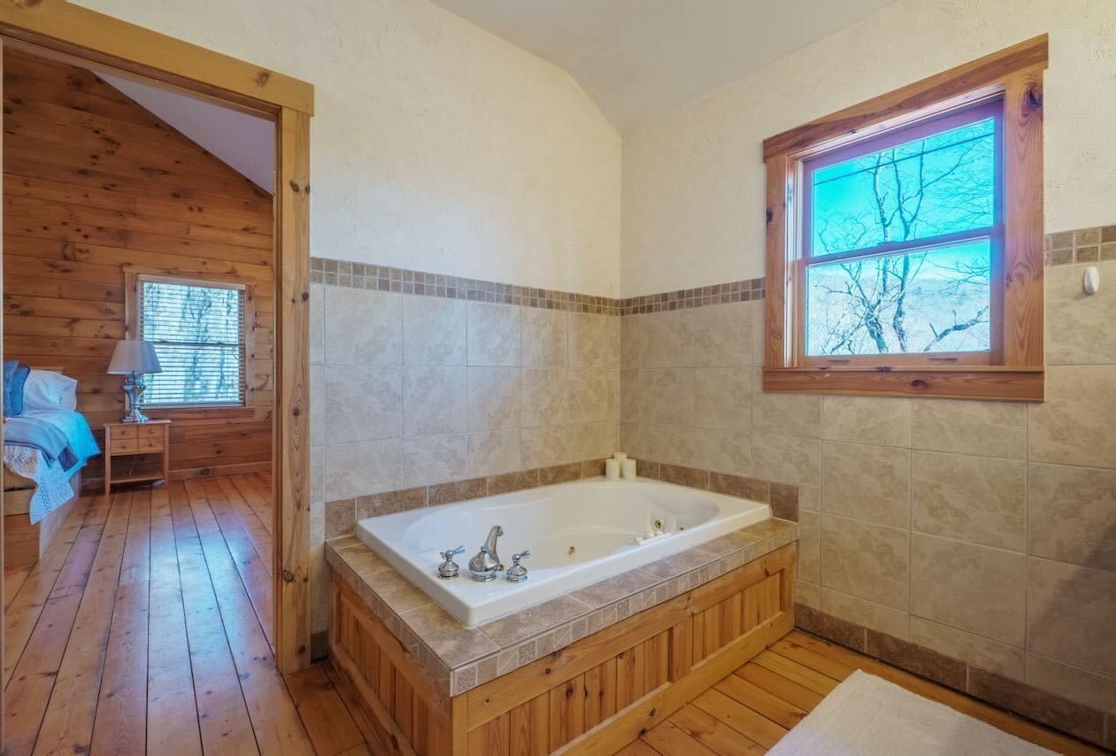 Une salle de bain avec une baignoire en bois, une fenêtre donnant sur un beau paysage et un plancher en bois.