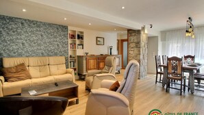 A spacious living room with a sofa, armchairs, a coffee table, and a dining area with a table and chairs. There is a bookshelf and a stone wall in the background. - Gîte Spacieux 3 Chambres, en Bord de Mer, Bretagne Sud, 56, Port-louis (Port-Louis)