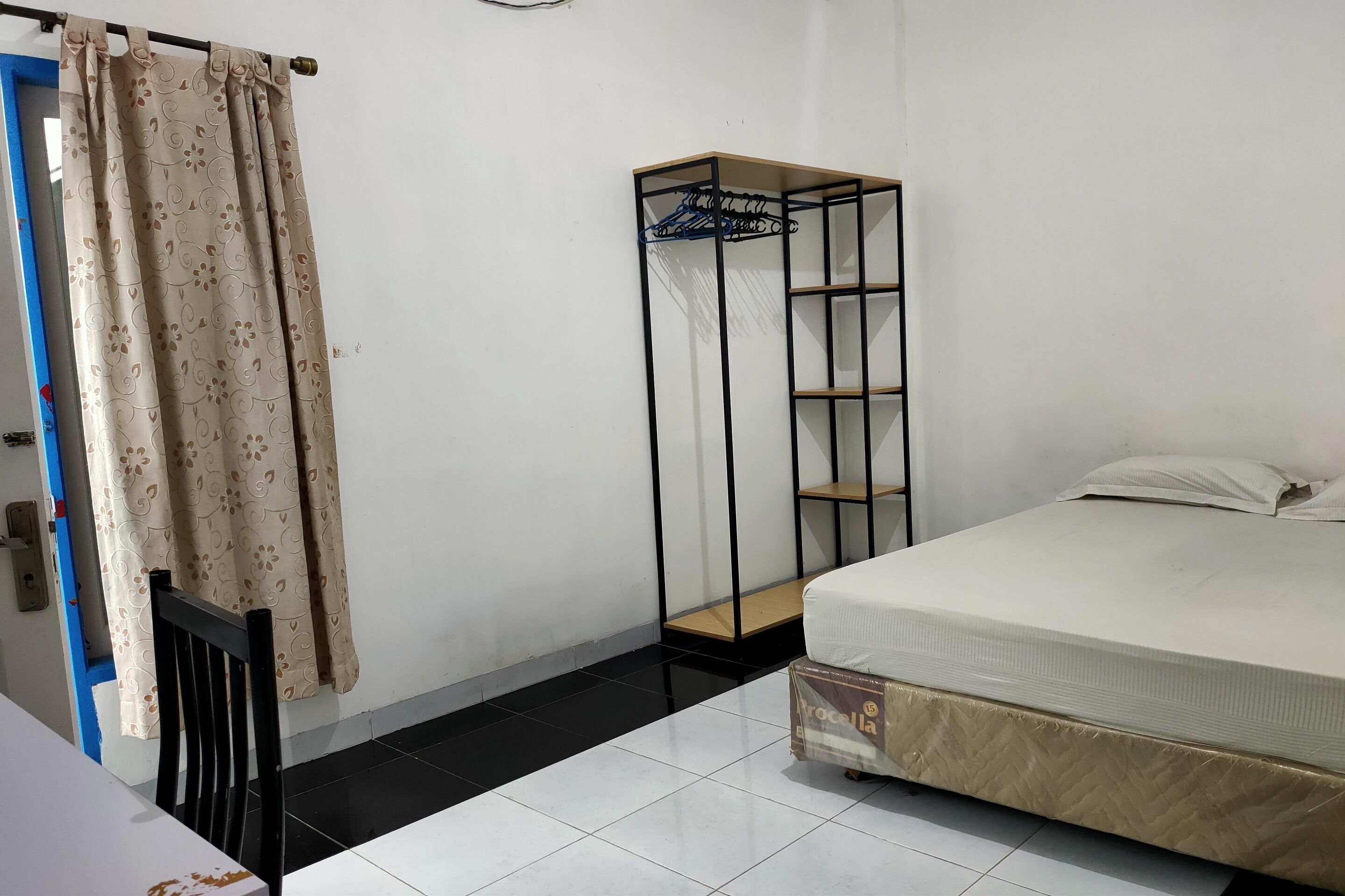 A room with a bed, a metal shelf unit, a chair, and a curtain.