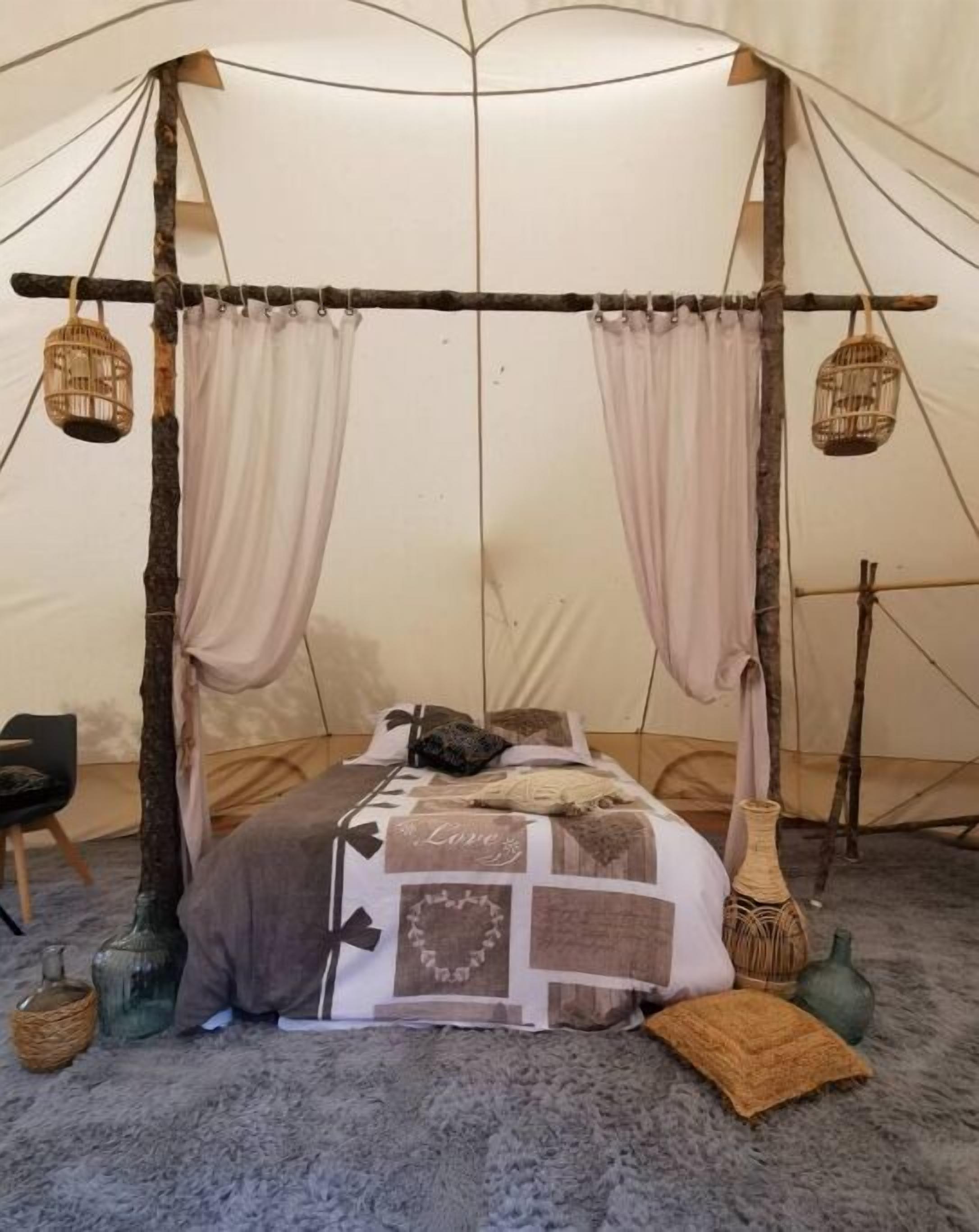 Un lit douillet avec une couverture à motifs, des rideaux tombants et des lanternes suspendues dans une pièce qui ressemble à une tente.