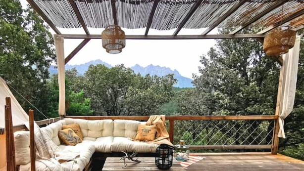 Ein gemütlicher Sitzbereich im Freien mit einer gepolsterten Couch und einem Holztisch, mit Blick auf eine gebirgige Landschaft.