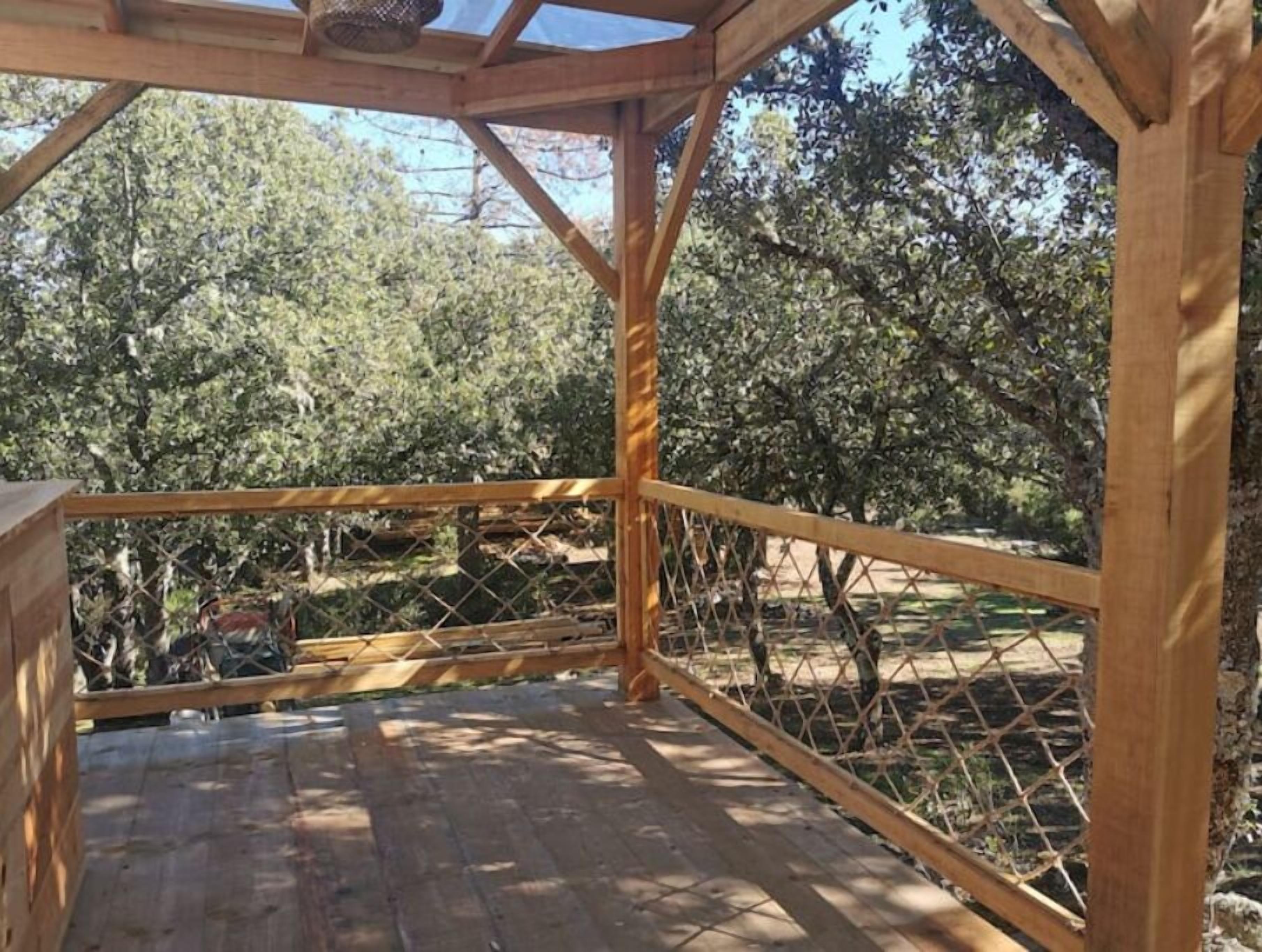 Un kiosque en bois avec une clôture en métal, entouré d’arbres.