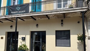 A building with a sign reading 'Herbert George Apartment Hotel,' featuring a balcony with metal railings, potted plants, and a light fixture. - Herbert George Apartment Hotel  (Clairac)