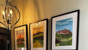 A wall with six framed posters of different towns, a white radiator, and a black door. - Herbert George Apartment Hotel  (Clairac)