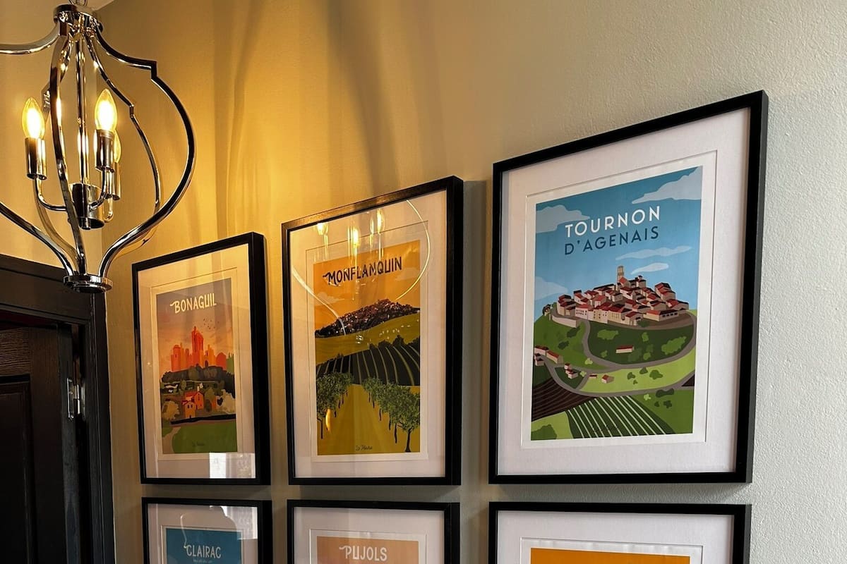 A wall with six framed posters of different towns, a white radiator, and a black door.