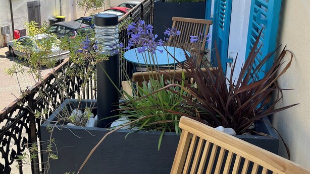 A narrow urban street with buildings on either side, a small outdoor seating area with a table and chairs, and a few parked cars. - Herbert George Apartment Hotel  (Clairac)
