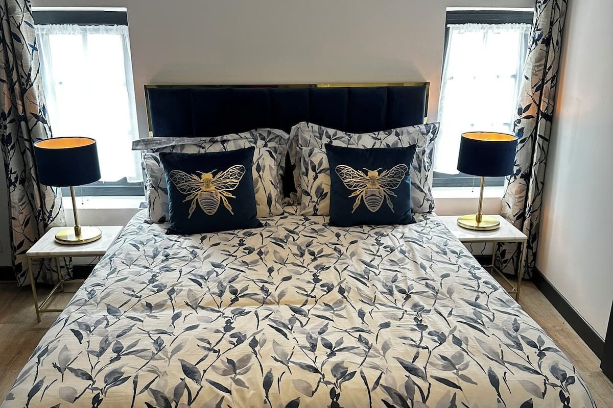 A large bed with a floral bedspread, two matching pillows, a dark headboard, and a bedside table with a lamp.