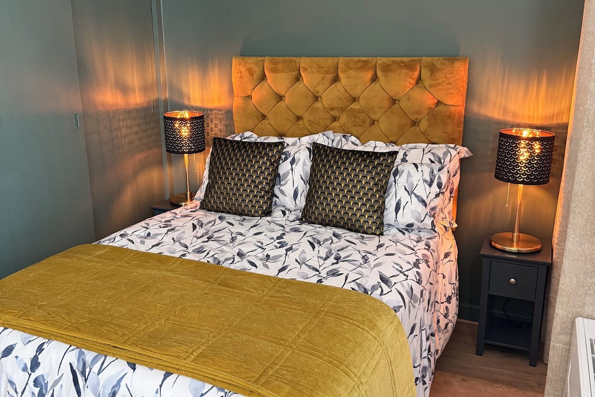 A bed with a tufted headboard, two bedside tables with lamps, and a floral-patterned bedspread.