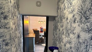 A hallway with patterned wallpaper, a wooden floor, and a table with a blue bowl and a white vase. - Herbert George Apartment Hotel  (Clairac)