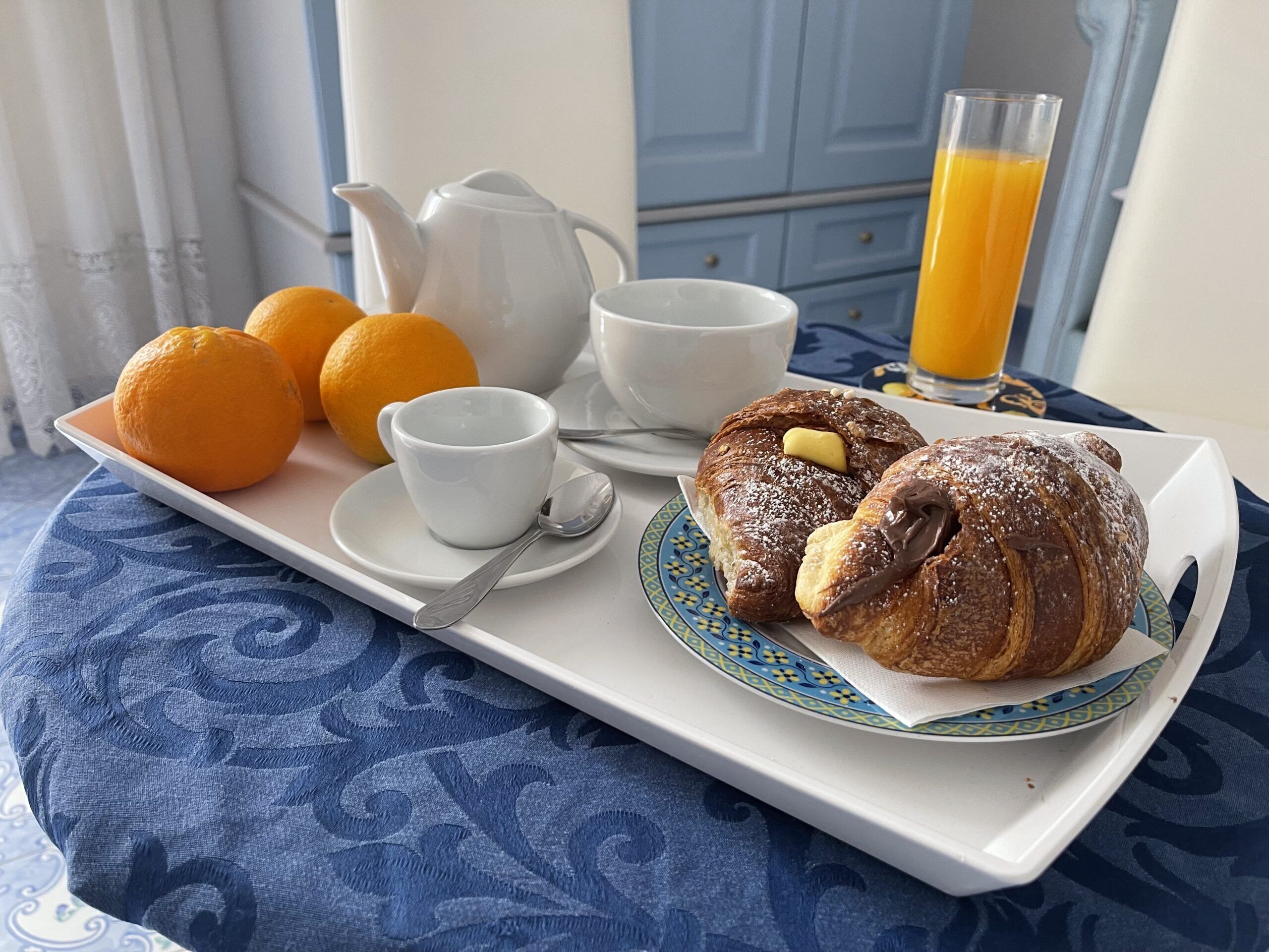 A breakfast tray with pastries, a teapot, a cup, a plate with oranges, and a glass of orange juice.